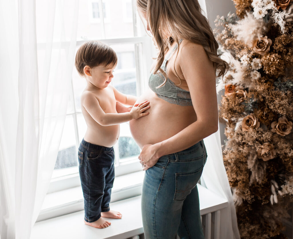 pregnant woman wearing jeans and bra with bare belly and little boy touching her belly by dc maternity photographer