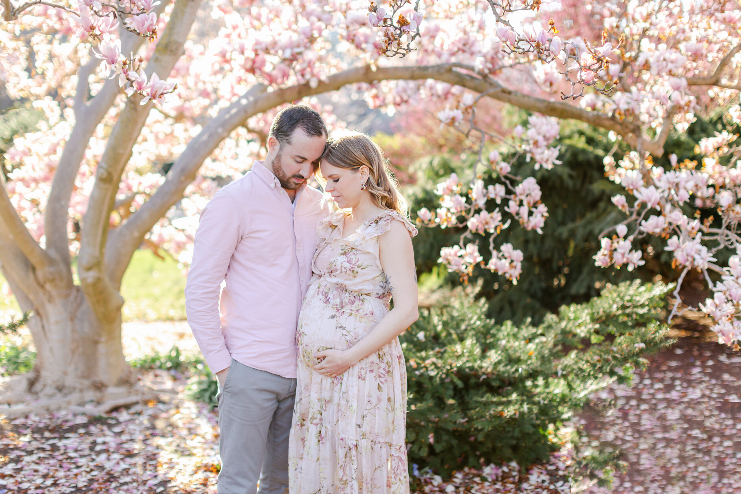 Expecting couple in garden with pink blooms