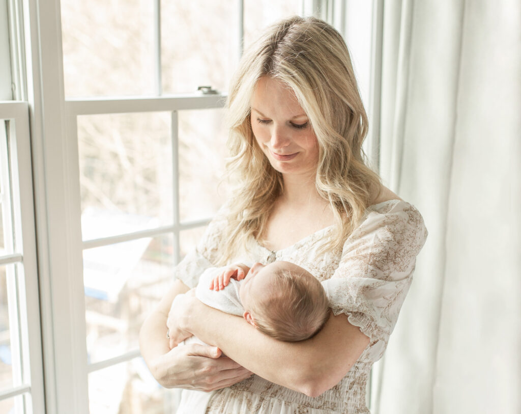 Woman looking lovingly down at her new baby in by a window with beautiful light